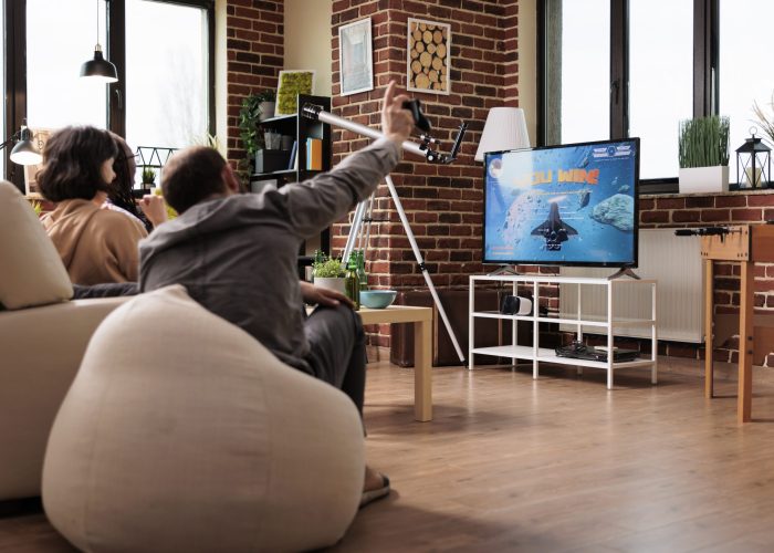 Multicultural people sitting on sofa in living room while playing space simulation games on console device. Diverse friends sitting at home while enjoying videogames together.