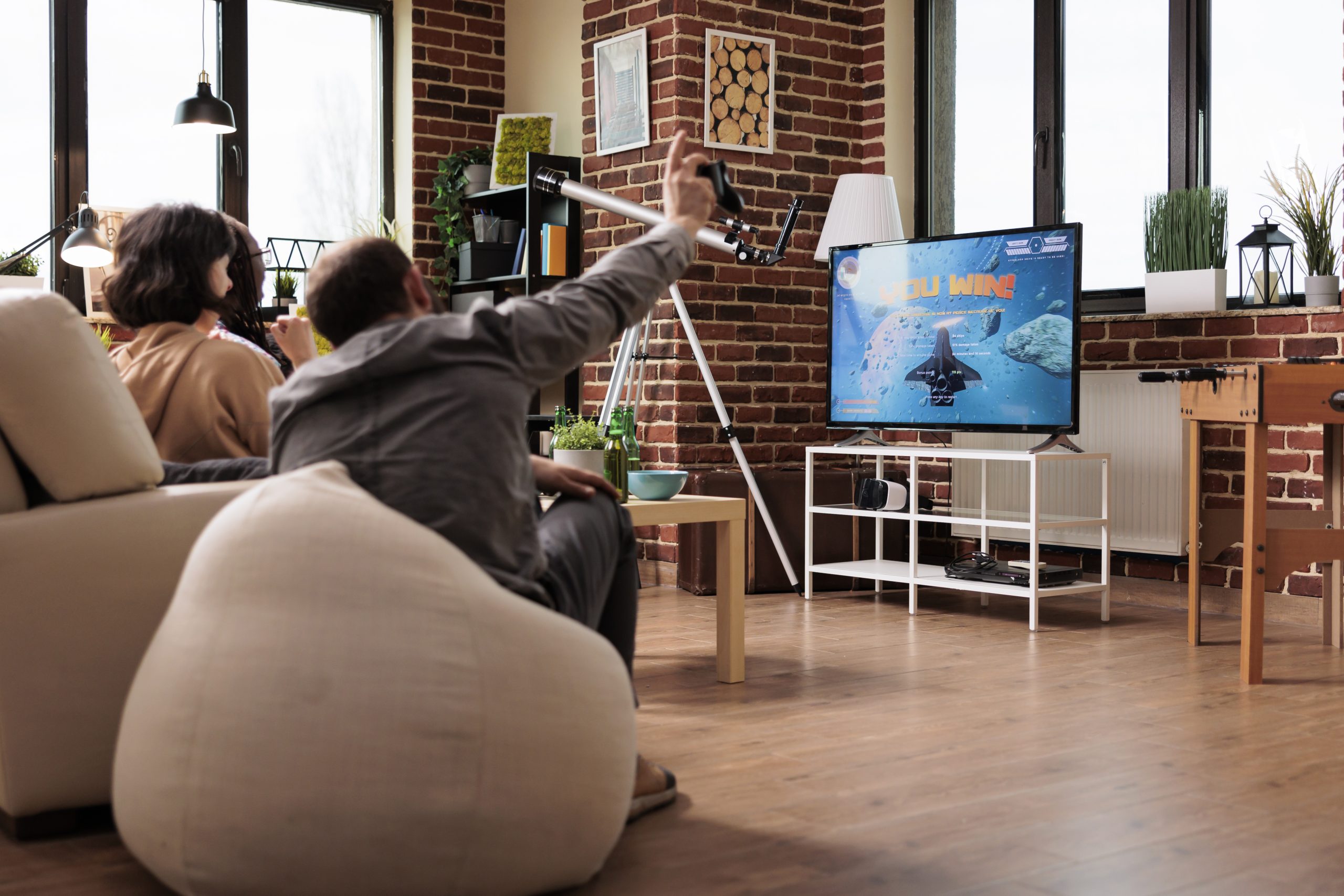 Multicultural people sitting on sofa in living room while playing space simulation games on console device. Diverse friends sitting at home while enjoying videogames together.